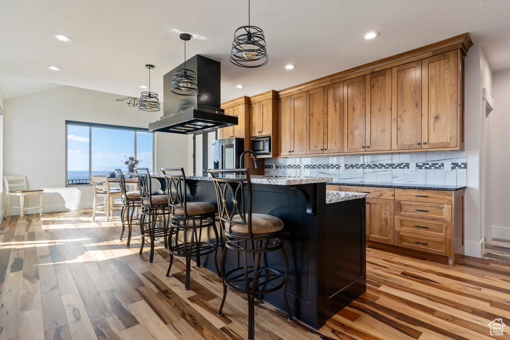 Kitchen featuring light wood-type flooring, backsplash, island range hood, and light stone counters