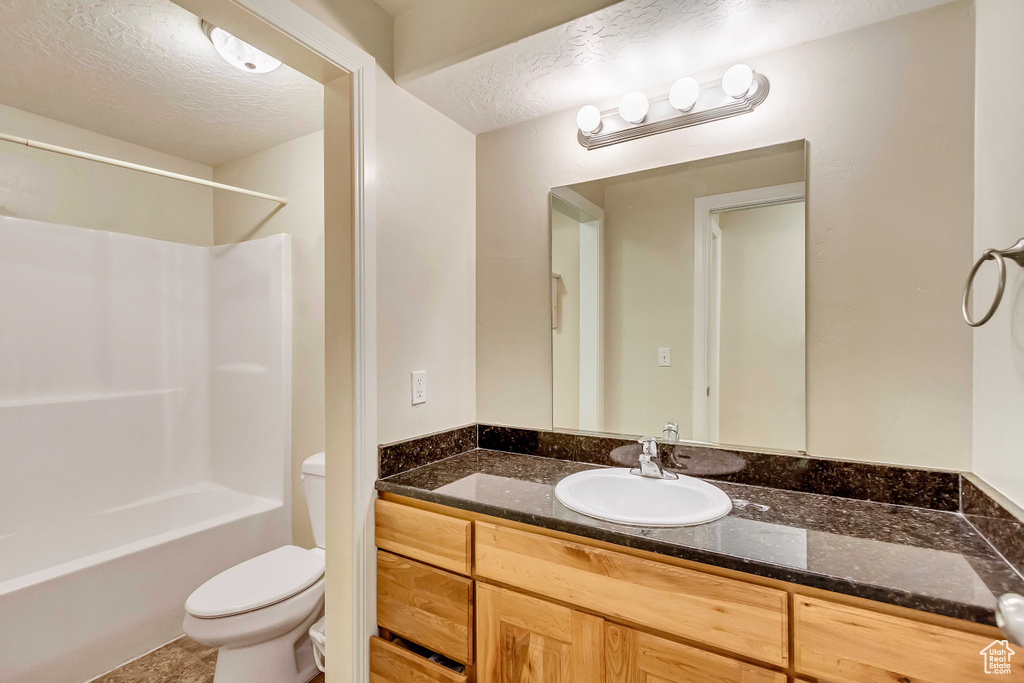 Full bathroom with vanity, toilet, a textured ceiling, and washtub / shower combination