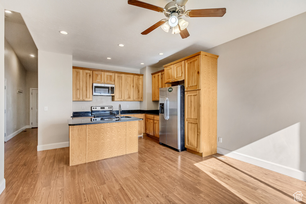 Kitchen with appliances with stainless steel finishes, a center island with sink, ceiling fan, light hardwood / wood-style floors, and sink