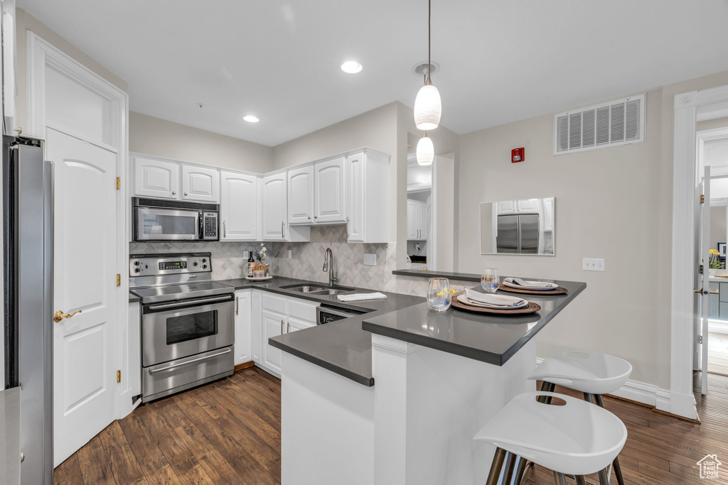 Kitchen featuring a kitchen bar, kitchen peninsula, dark wood-type flooring, and stainless steel appliances