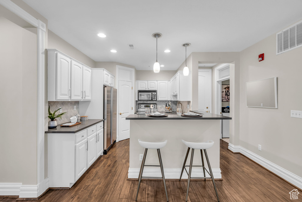 Kitchen with dark hardwood / wood-style flooring, stainless steel appliances, white cabinets, and backsplash