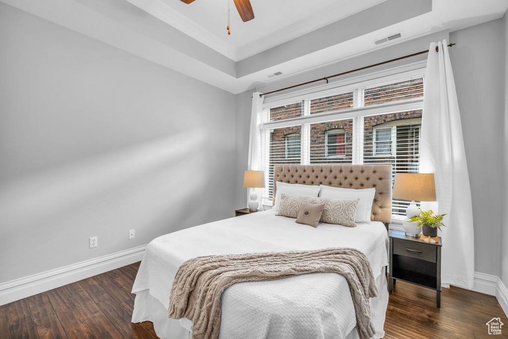 Bedroom featuring dark hardwood / wood-style flooring, ceiling fan, a raised ceiling, and ornamental molding