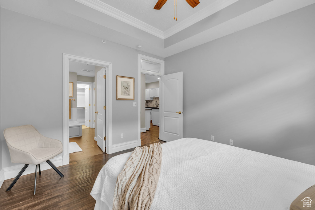 Bedroom with a tray ceiling, dark wood-type flooring, ensuite bathroom, and ceiling fan
