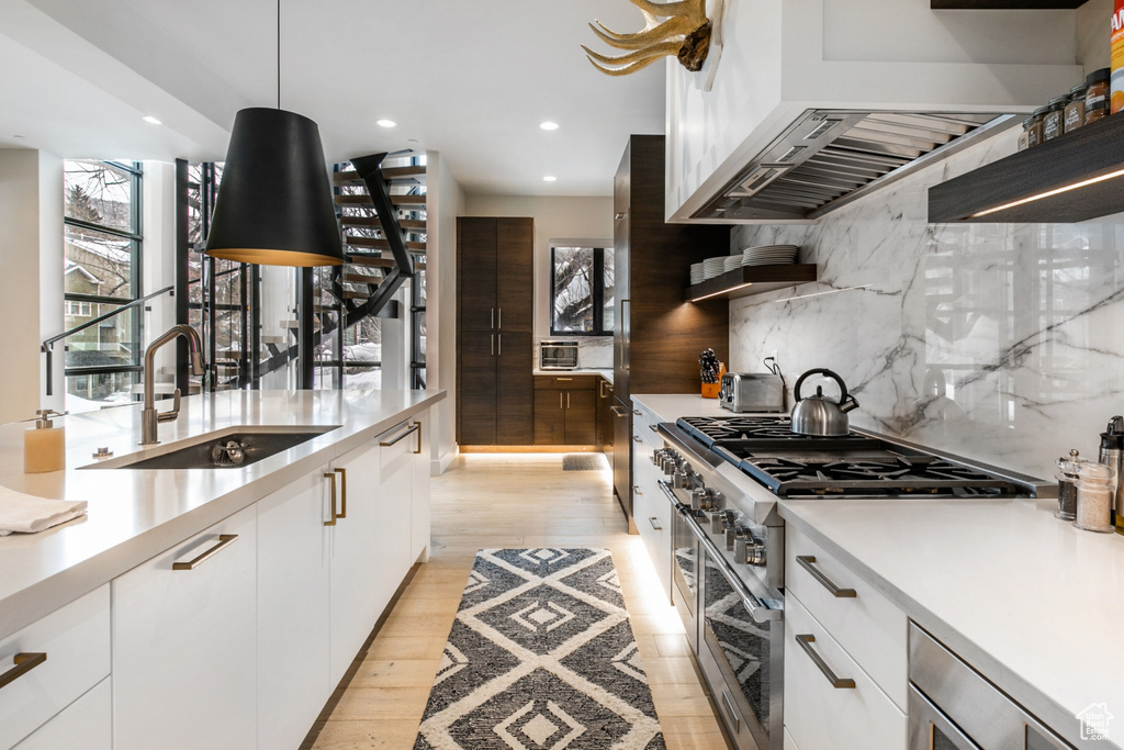 Kitchen featuring white cabinetry, tasteful backsplash, light hardwood / wood-style floors, range with two ovens, and sink
