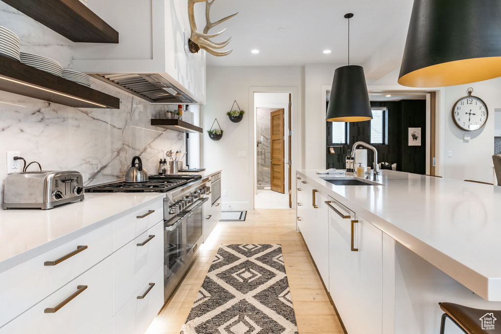 Kitchen with white cabinetry, range with two ovens, decorative backsplash, sink, and light hardwood / wood-style floors