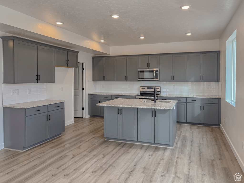 Kitchen featuring appliances with stainless steel finishes, light hardwood / wood-style floors, gray cabinetry, and backsplash