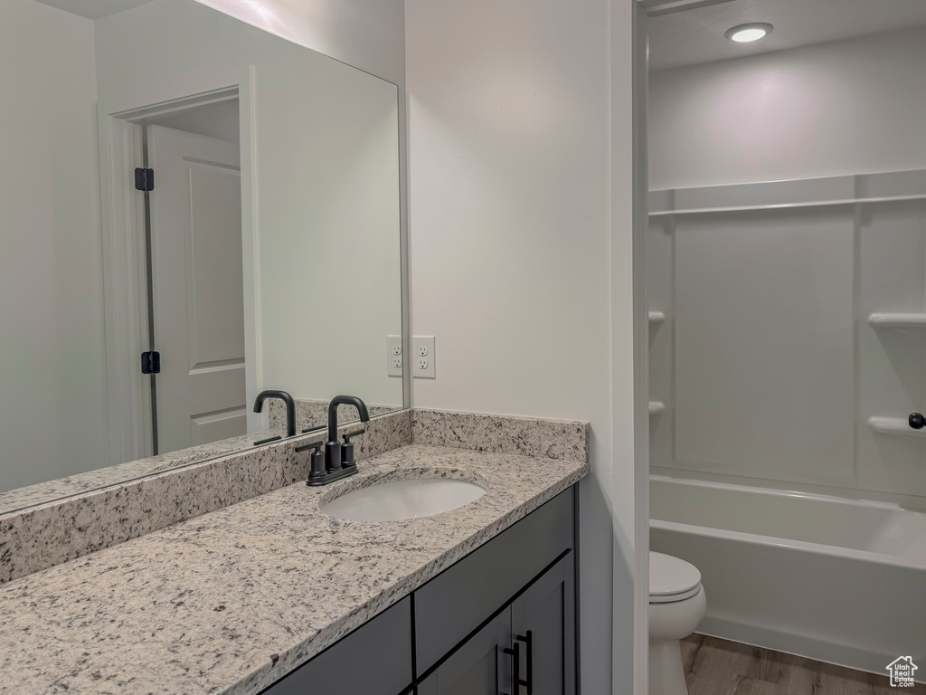 Full bathroom with  shower combination, toilet, vanity with extensive cabinet space, and hardwood / wood-style floors