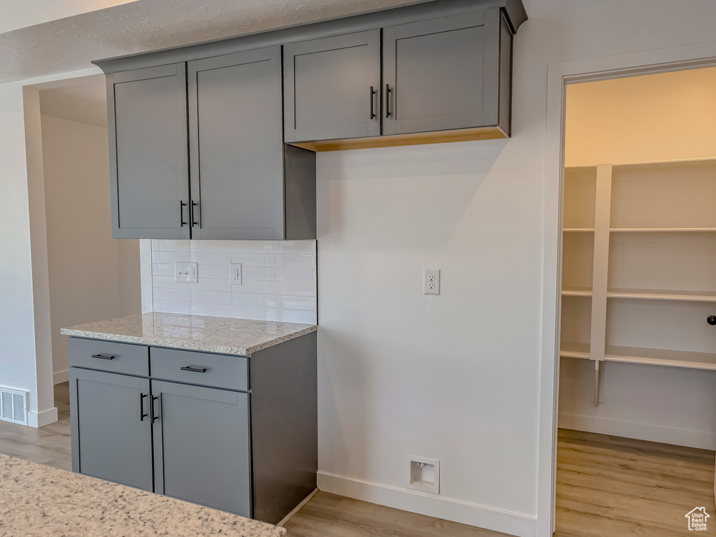 Kitchen with gray cabinets, light wood-type flooring, tasteful backsplash, and light stone countertops
