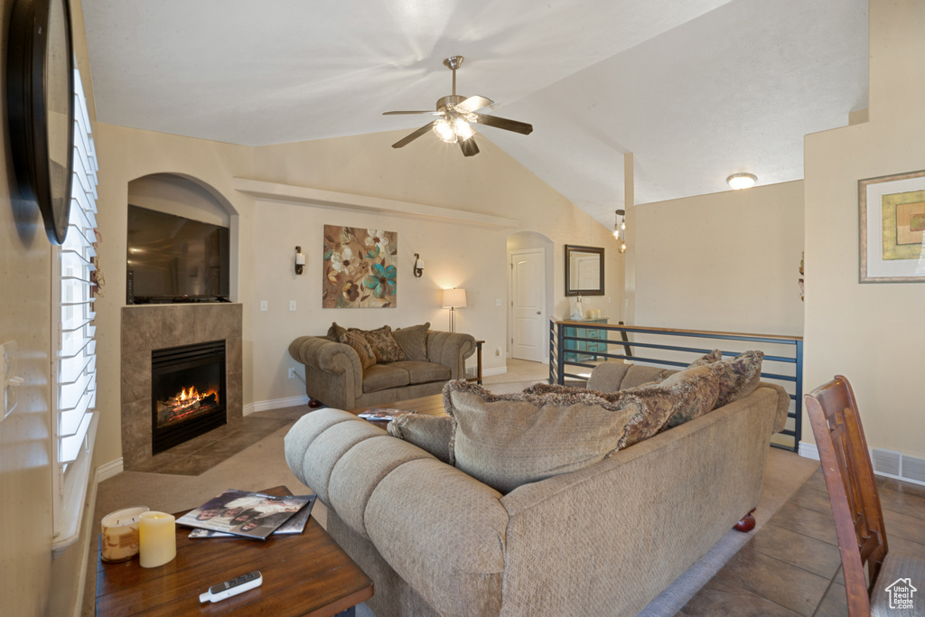 Living room featuring a tile fireplace, lofted ceiling, dark tile floors, and ceiling fan