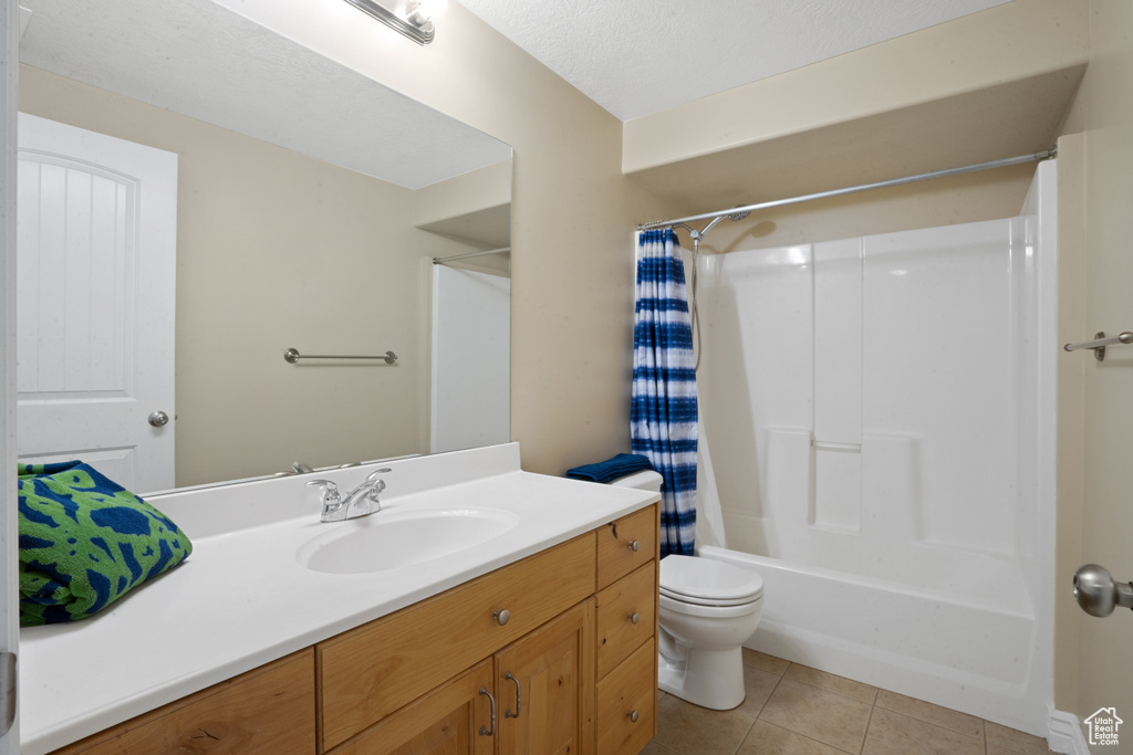 Full bathroom with a textured ceiling, shower / bath combination with curtain, tile floors, oversized vanity, and toilet