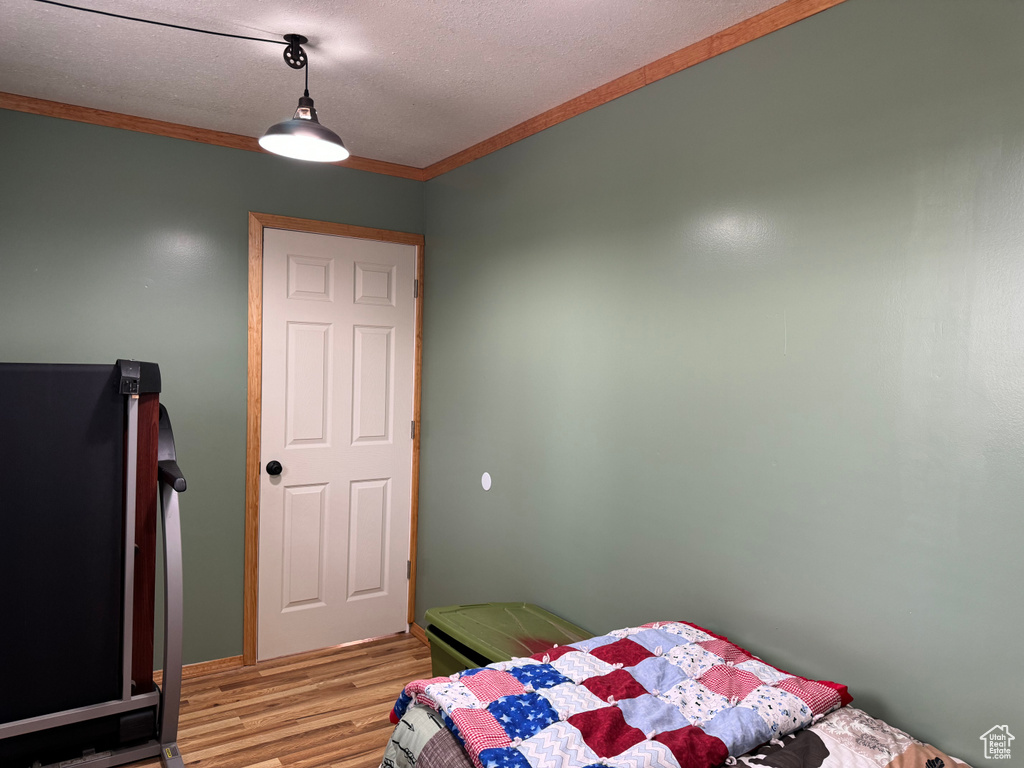 Bedroom with a textured ceiling, crown molding, and light hardwood / wood-style flooring