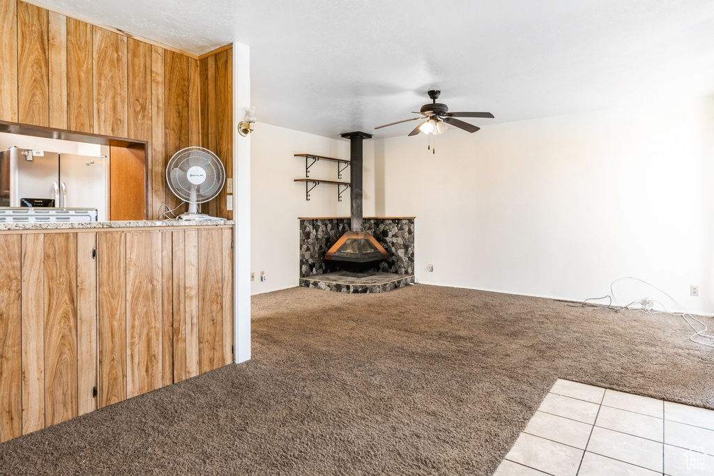 Unfurnished living room featuring a wood stove, light carpet, ceiling fan, and wood walls