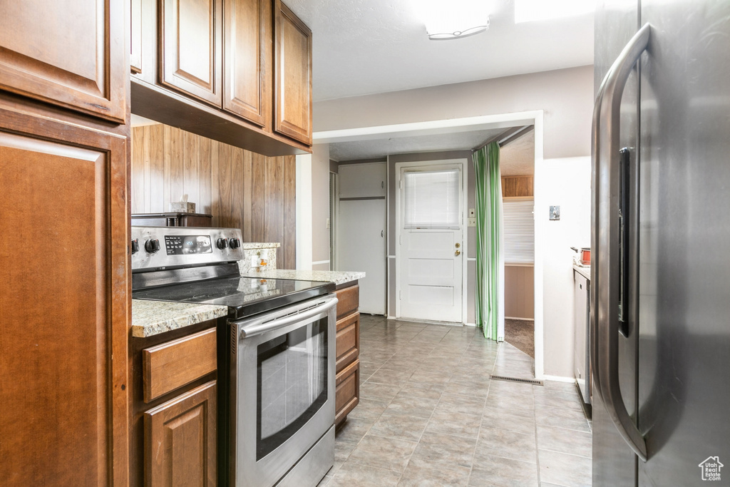 Kitchen with light tile floors, stainless steel appliances, and light stone counters