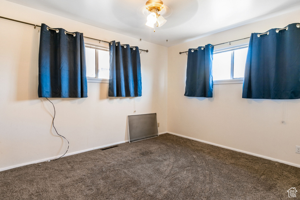 Spare room featuring dark colored carpet, a healthy amount of sunlight, and ceiling fan