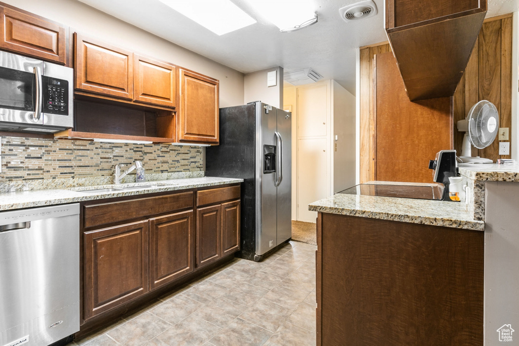 Kitchen with sink, appliances with stainless steel finishes, backsplash, light tile floors, and light stone counters