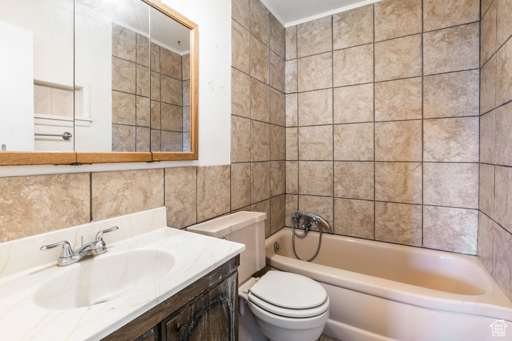 Full bathroom featuring vanity, toilet, tiled shower / bath, and tile walls