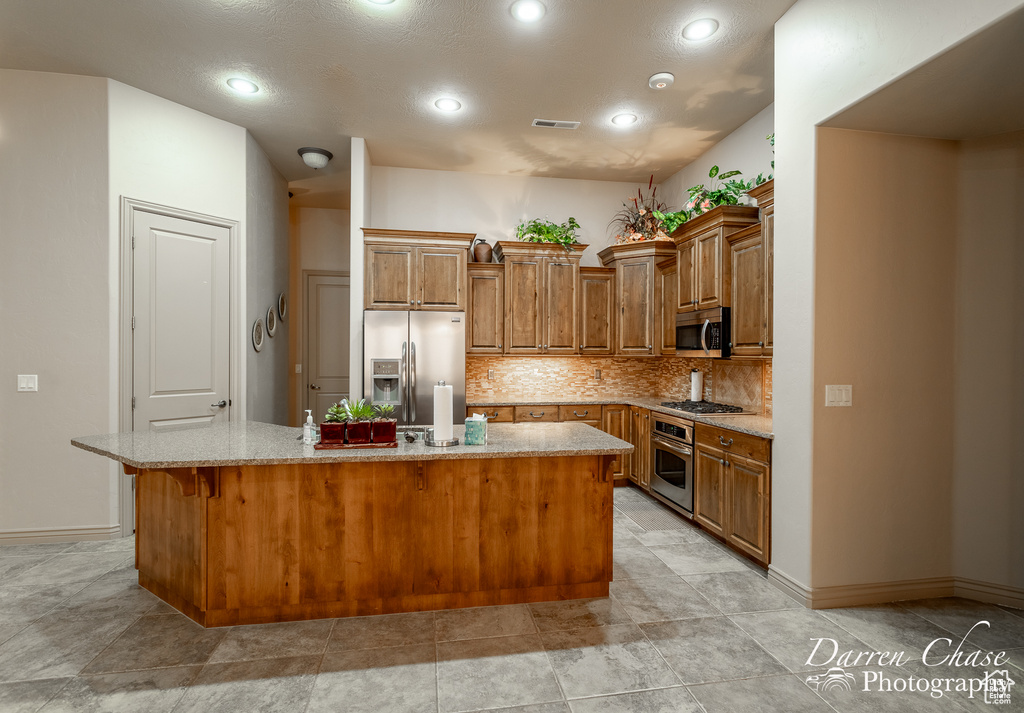 Kitchen with backsplash, stainless steel appliances, a kitchen island with sink, a breakfast bar, and light stone countertops