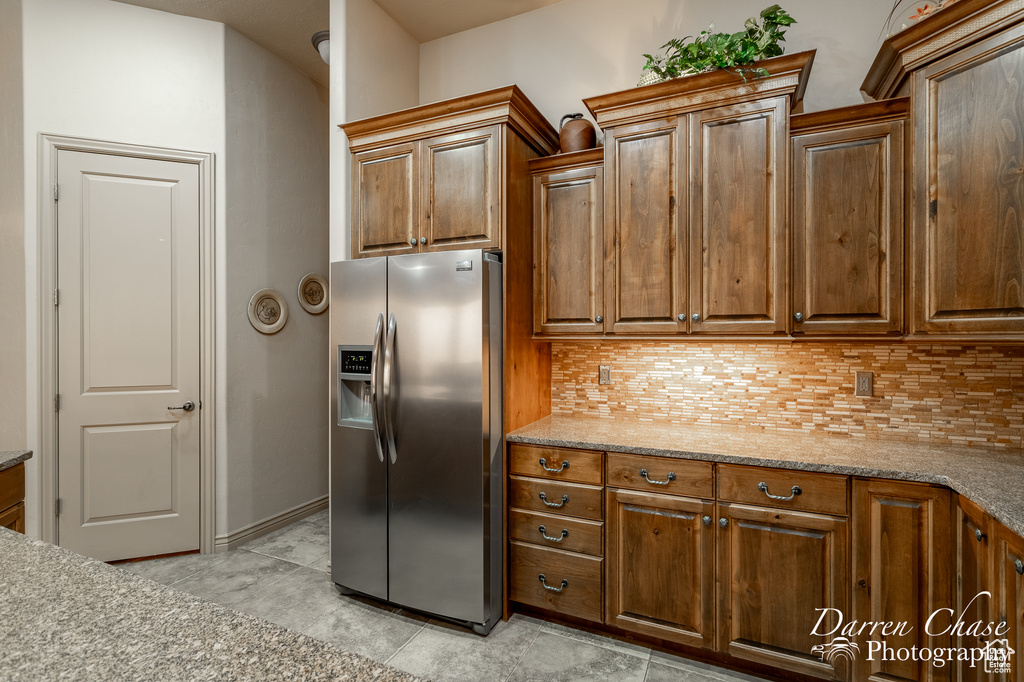 Kitchen featuring stainless steel fridge with ice dispenser, backsplash, light tile floors, and light stone counters
