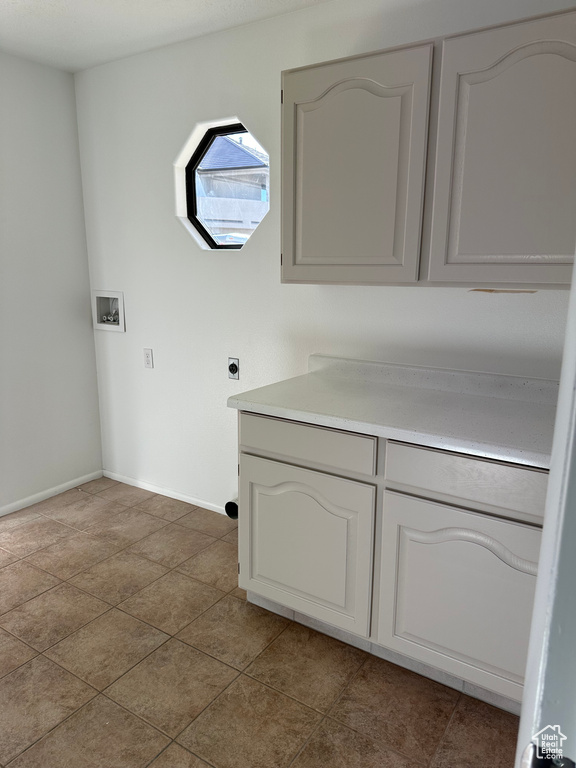 Laundry room with electric dryer hookup, cabinets, and tile floors