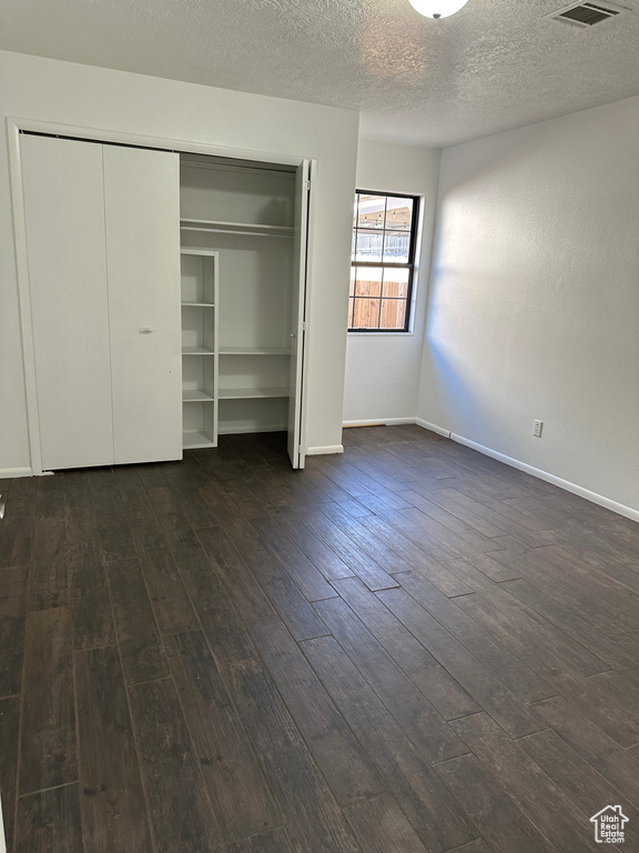 Unfurnished bedroom with dark hardwood / wood-style flooring, a textured ceiling, and a closet