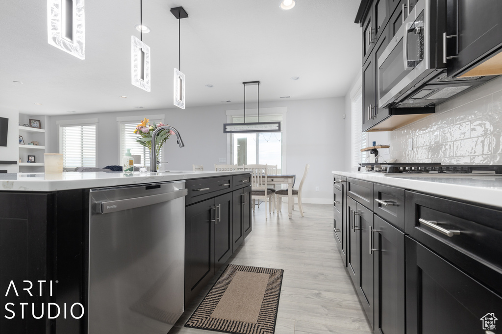Kitchen featuring tasteful backsplash, appliances with stainless steel finishes, hanging light fixtures, light wood-type flooring, and a center island