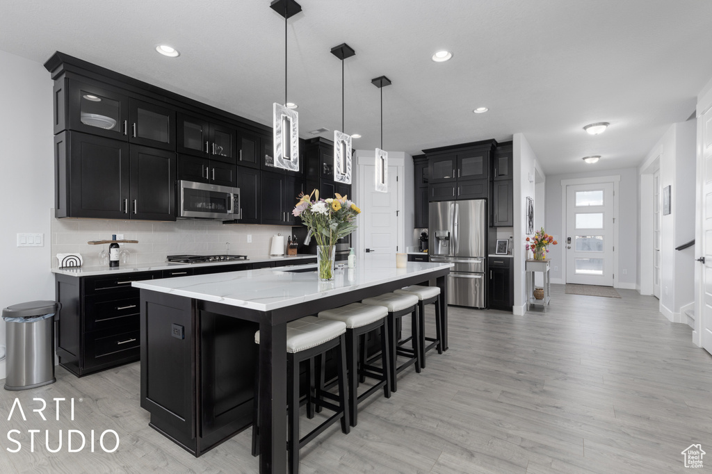 Kitchen with appliances with stainless steel finishes, a kitchen breakfast bar, light hardwood / wood-style flooring, pendant lighting, and a center island