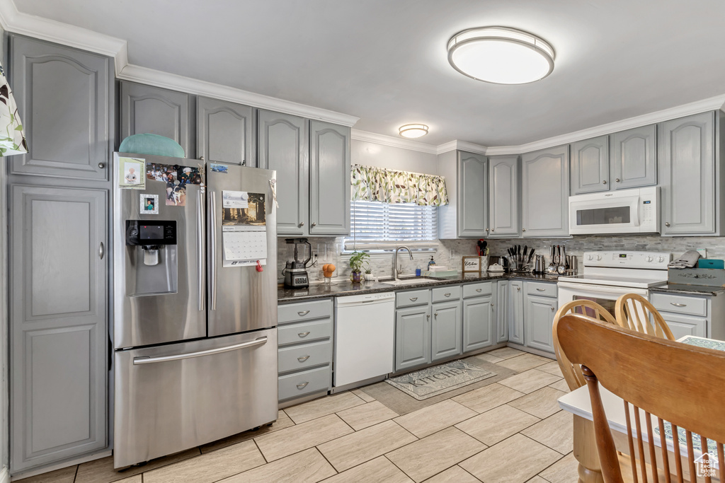 Kitchen with tasteful backsplash, gray cabinetry, light tile floors, white appliances, and sink