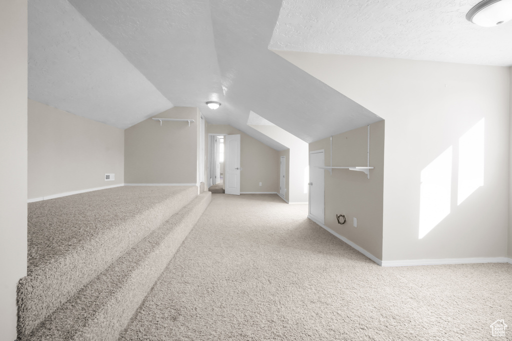 Bonus room featuring lofted ceiling, light carpet, and a textured ceiling