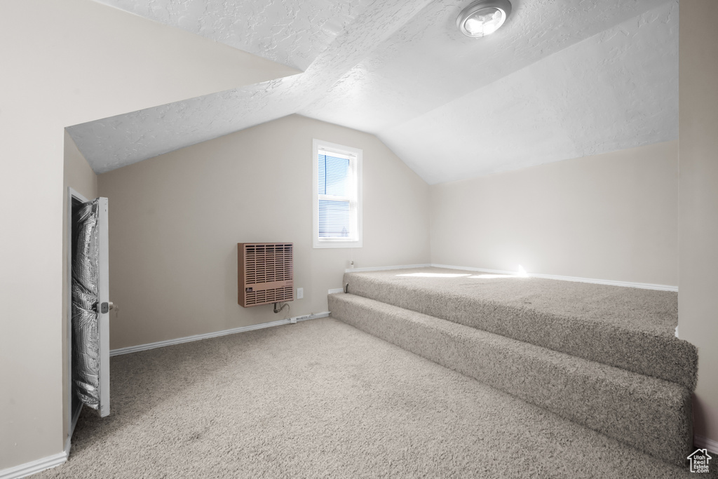 Bonus room with light colored carpet, a textured ceiling, and lofted ceiling