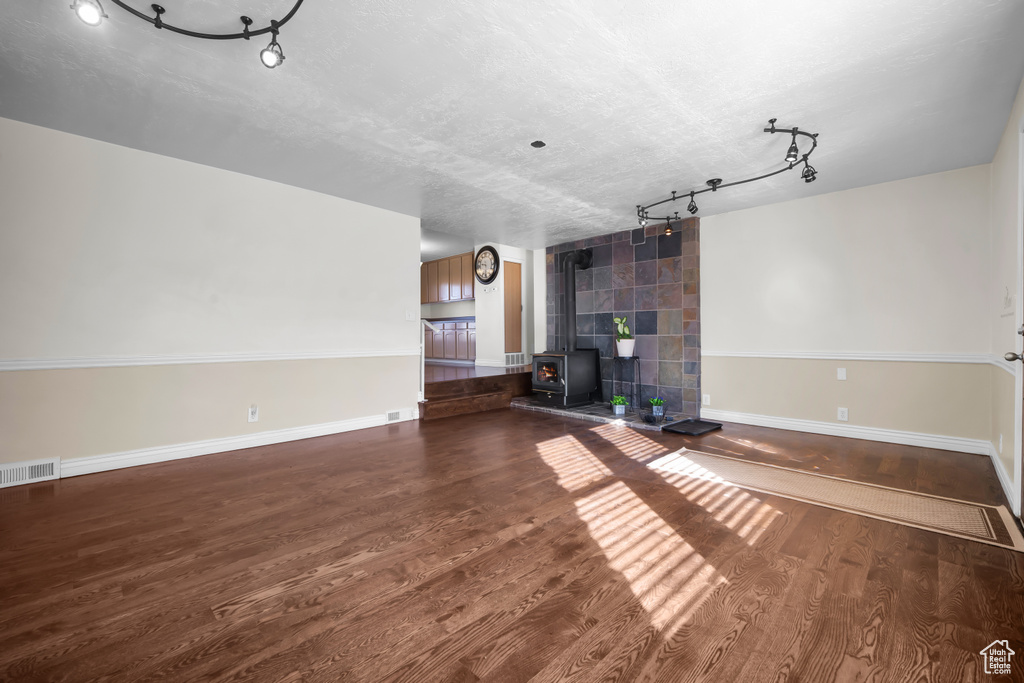Unfurnished living room featuring track lighting, a wood stove, a textured ceiling, and dark wood-type flooring