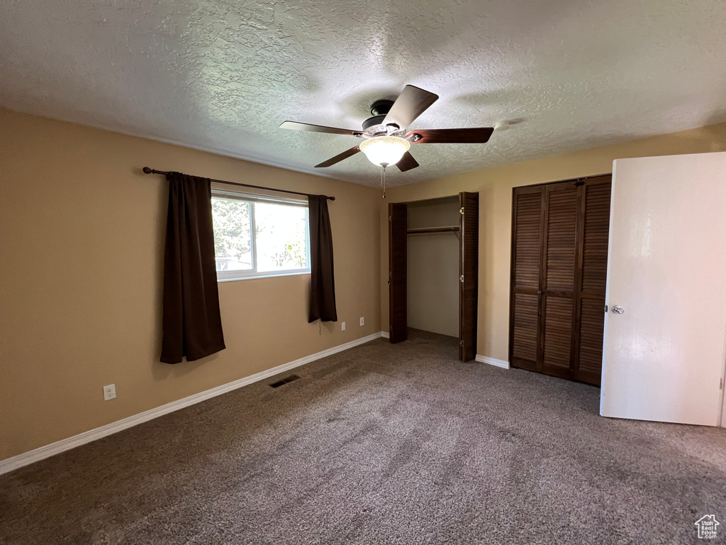 Unfurnished bedroom with dark colored carpet, a textured ceiling, multiple closets, and ceiling fan