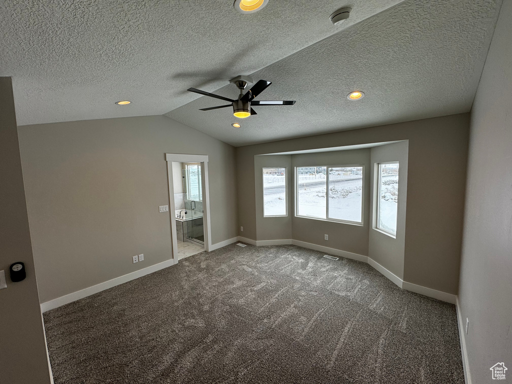 Carpeted empty room featuring a textured ceiling, lofted ceiling, and ceiling fan