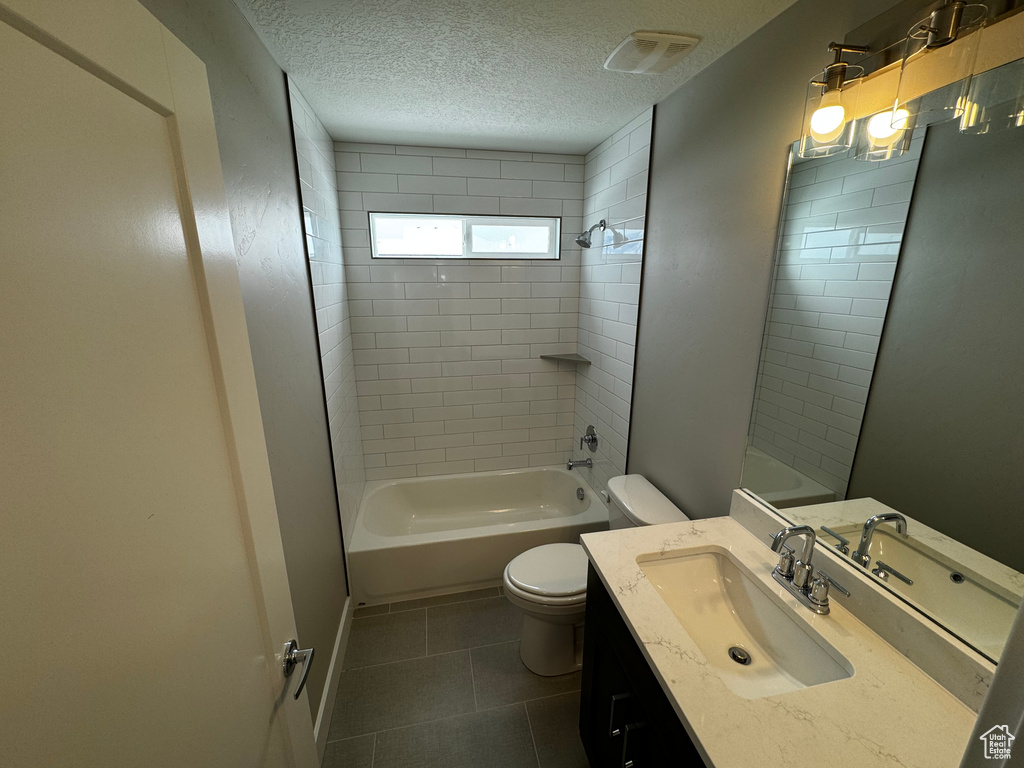 Full bathroom featuring tiled shower / bath combo, vanity with extensive cabinet space, a textured ceiling, toilet, and tile floors