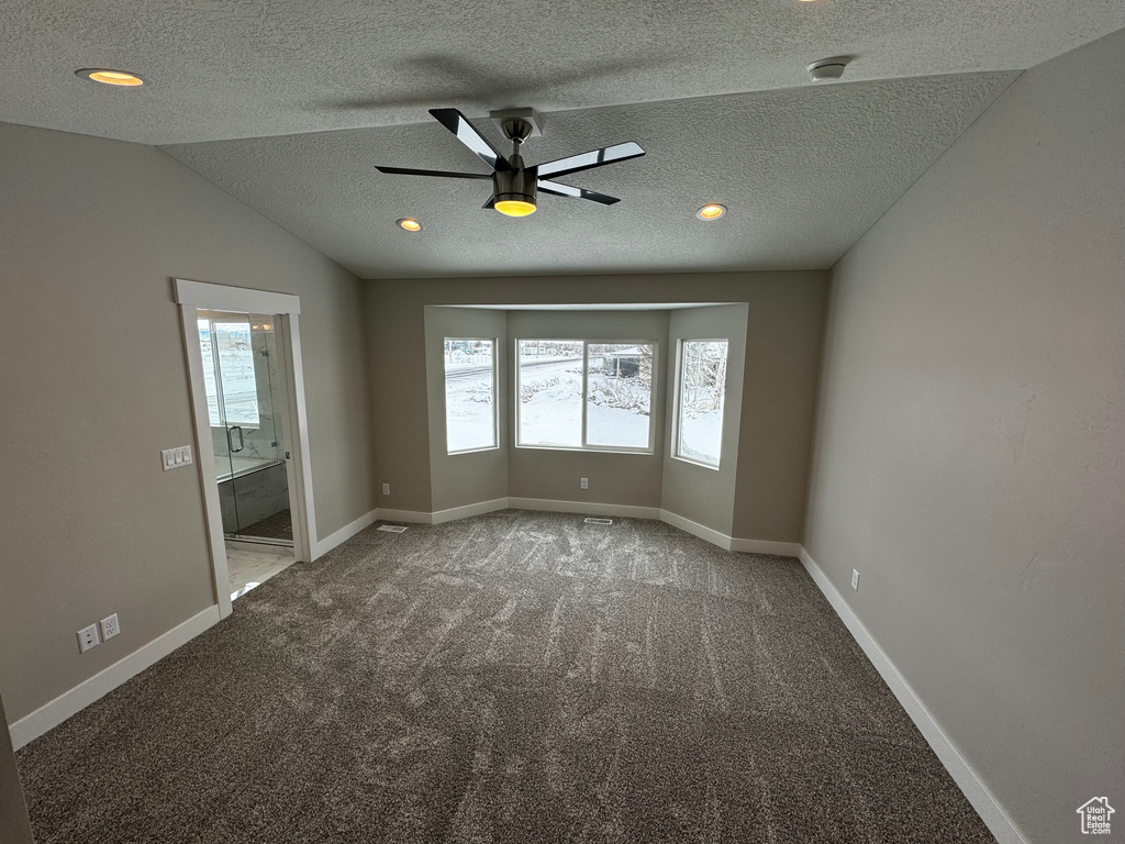 Carpeted empty room featuring a textured ceiling, ceiling fan, and lofted ceiling