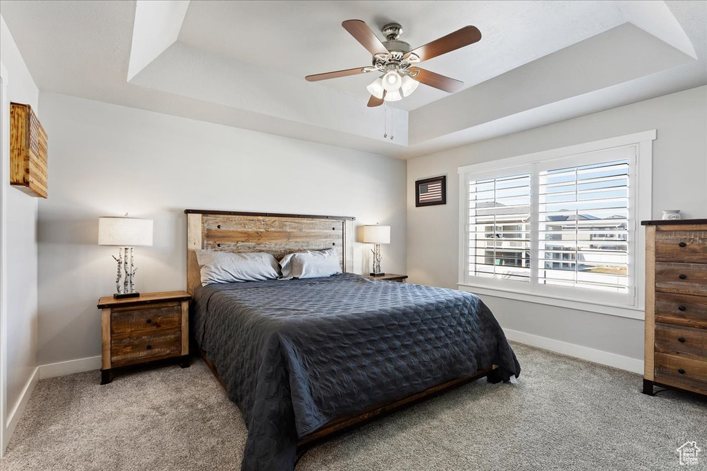 Bedroom with light colored carpet, a tray ceiling, and ceiling fan