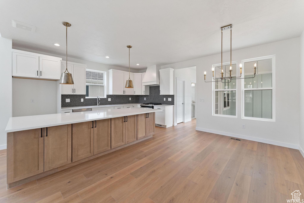 Kitchen featuring custom range hood, decorative light fixtures, a center island, and light hardwood / wood-style floors