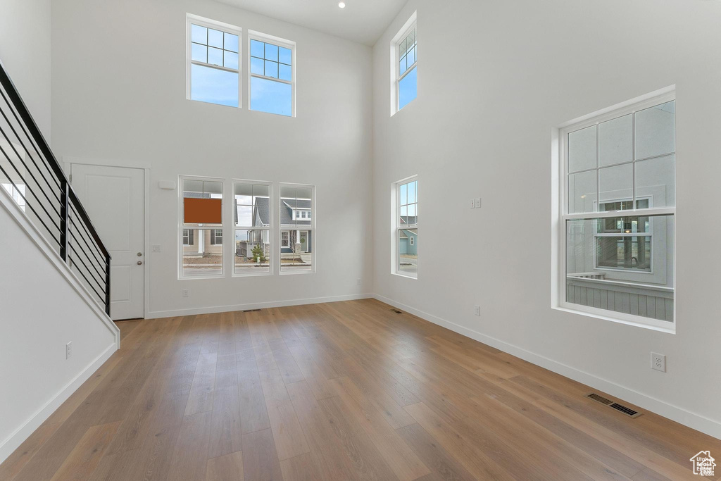 Unfurnished living room featuring a high ceiling, a healthy amount of sunlight, and light hardwood / wood-style flooring