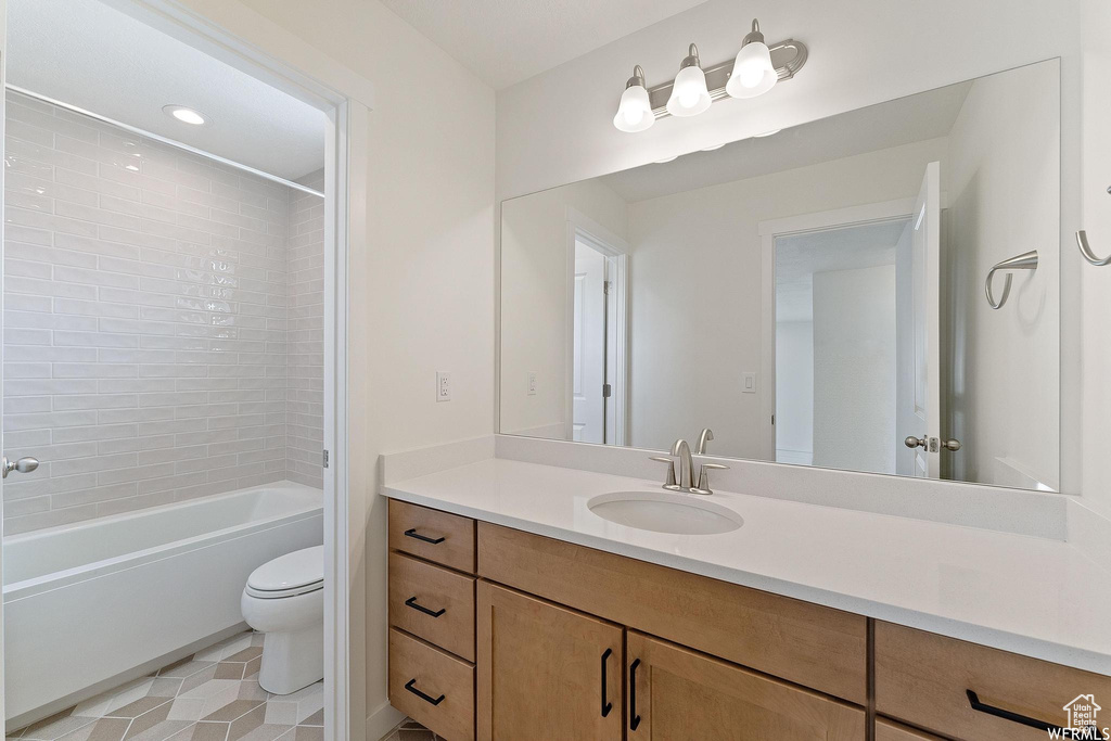 Full bathroom featuring tiled shower / bath combo, toilet, vanity with extensive cabinet space, and tile floors