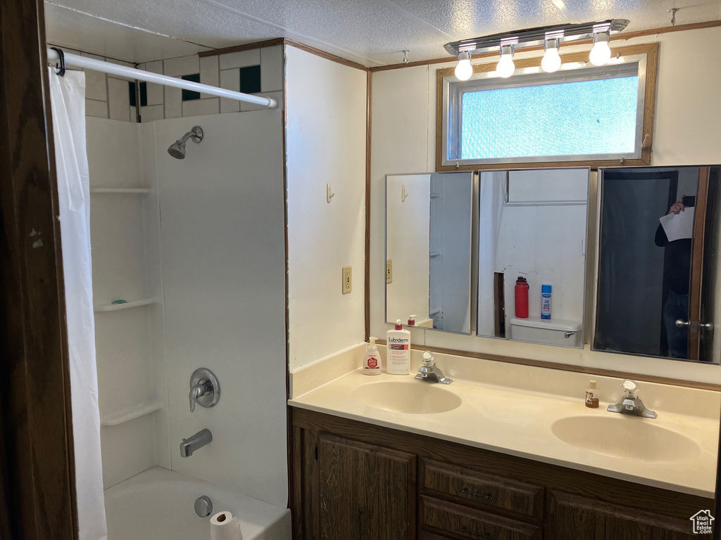 Full bathroom with dual sinks, a textured ceiling, shower / tub combo with curtain, vanity with extensive cabinet space, and toilet