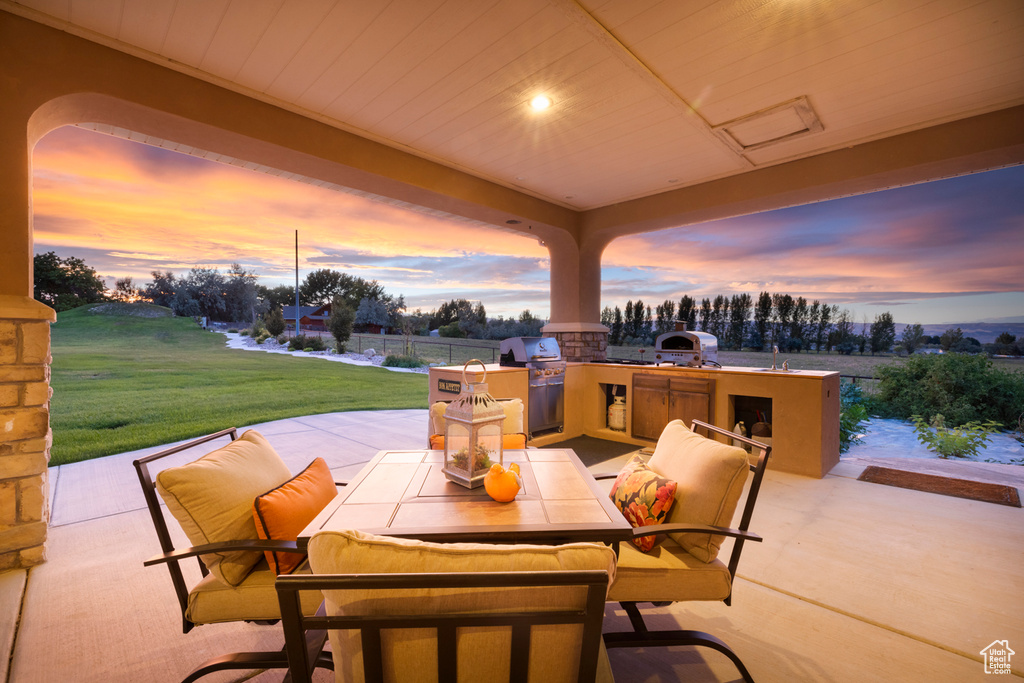 Patio terrace at dusk featuring exterior kitchen and a grill