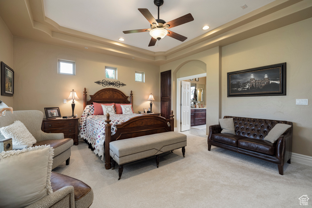 Bedroom with ensuite bathroom, light carpet, a tray ceiling, and ceiling fan