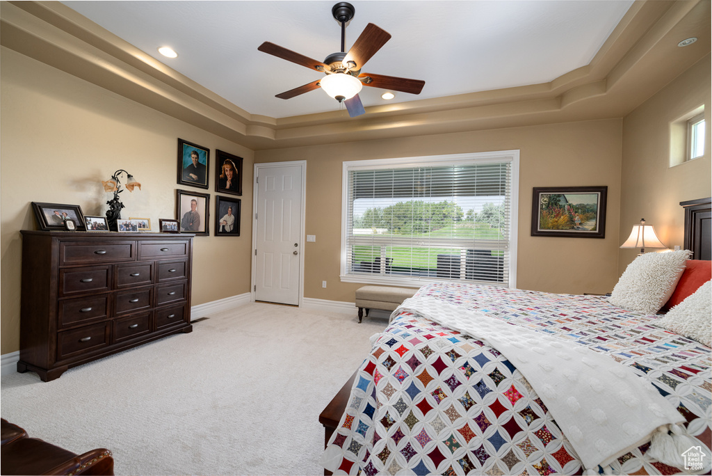 Carpeted bedroom featuring multiple windows, ceiling fan, and a tray ceiling