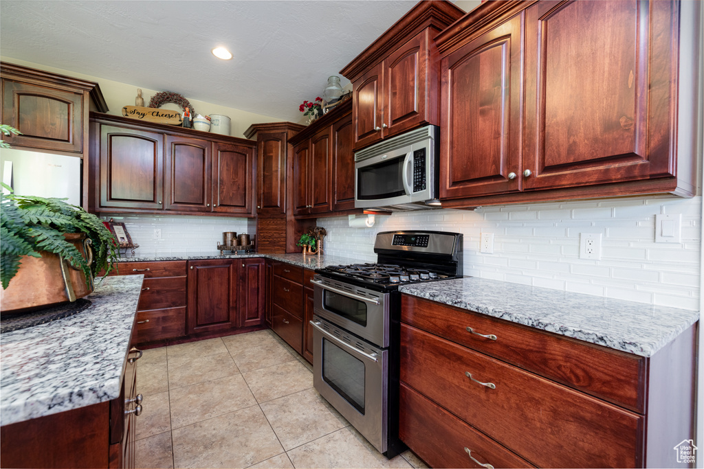 Kitchen featuring backsplash, stainless steel appliances, light tile floors, and light stone countertops
