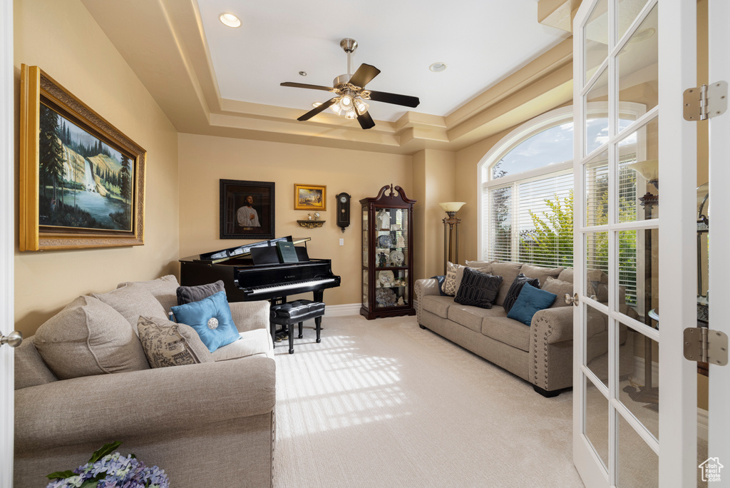 Living room with a raised ceiling, light colored carpet, and ceiling fan