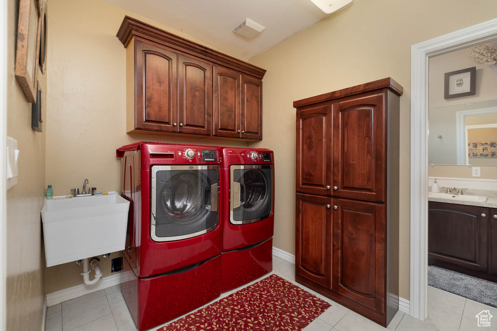 Washroom with independent washer and dryer, light tile floors, sink, and cabinets