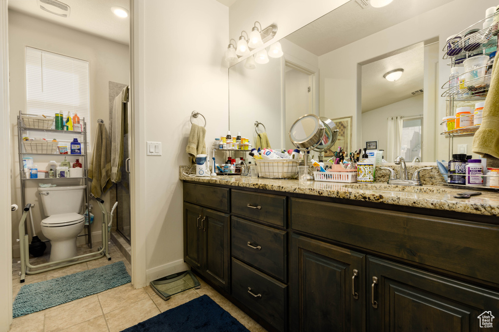 Bathroom featuring double sink, toilet, vanity with extensive cabinet space, and tile flooring