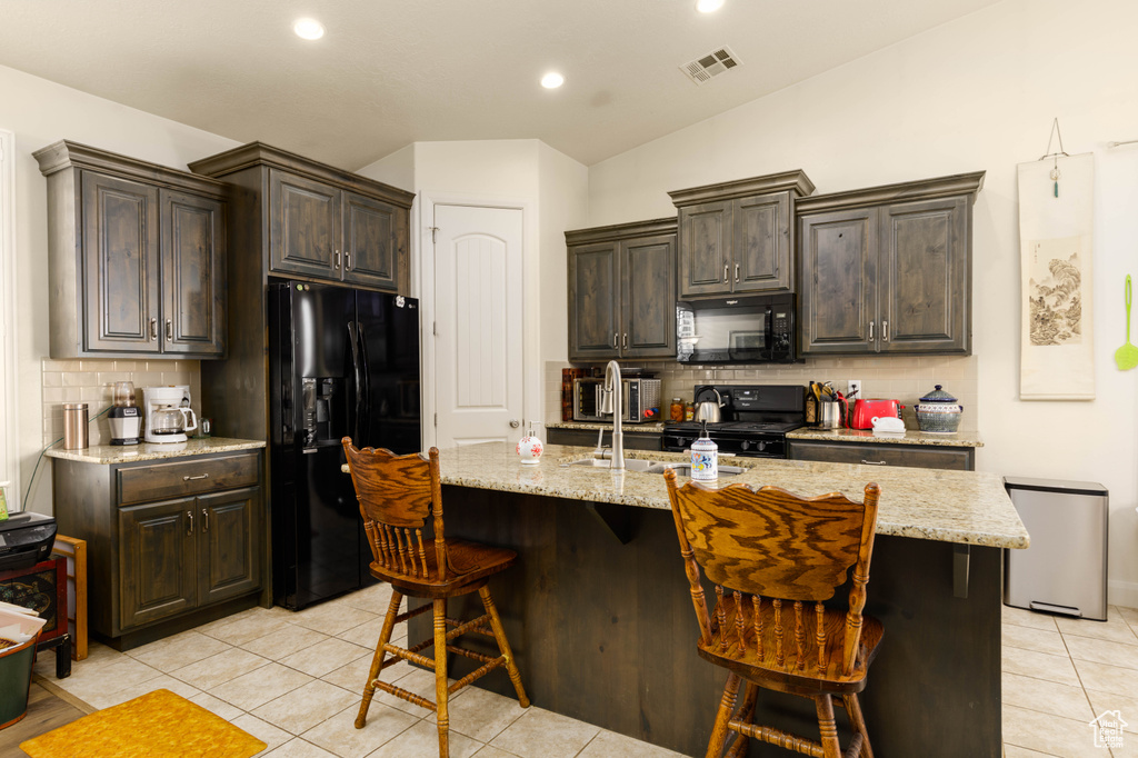 Kitchen with black appliances, light tile flooring, a kitchen breakfast bar, and a kitchen island with sink