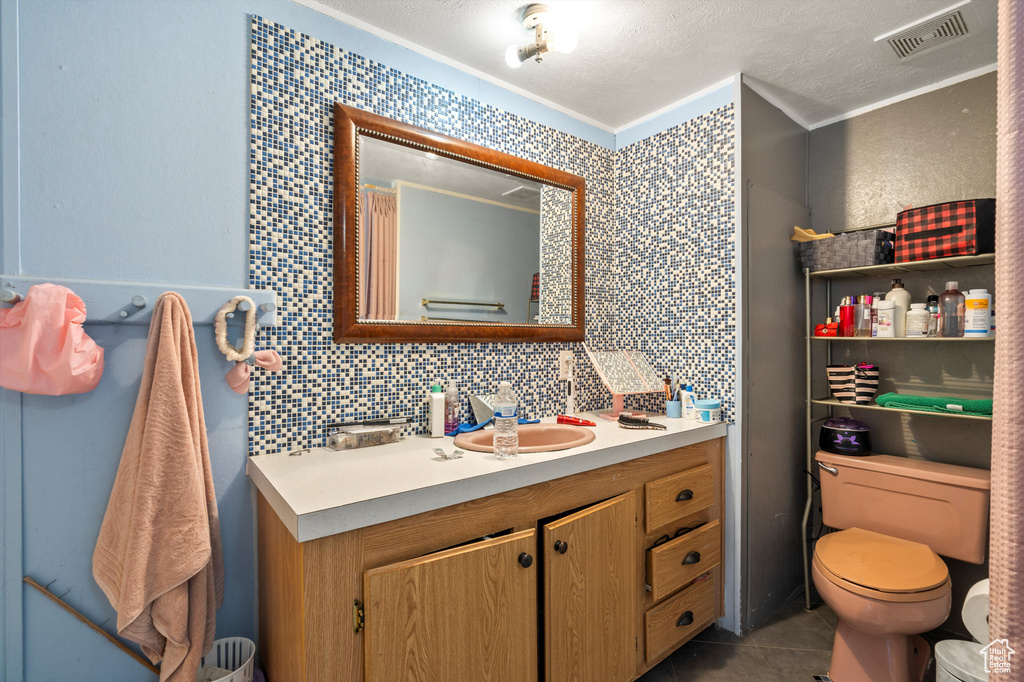 Bathroom featuring a textured ceiling, backsplash, vanity, toilet, and tile flooring