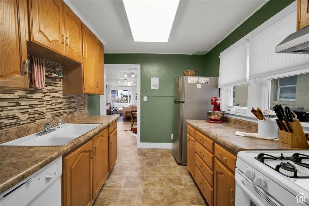Kitchen featuring tasteful backsplash, custom range hood, light tile flooring, white appliances, and sink