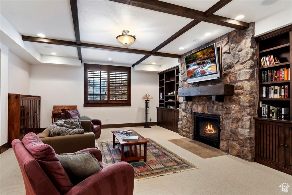 Living room with built in features, a stone fireplace, light colored carpet, and beam ceiling